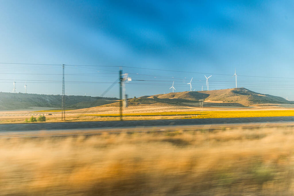 Tren raylarında hızla ilerlerken güneşli arazilere bakıyorum. Uzakta rüzgâr tarlaları.. - Fotoğraf, Görsel