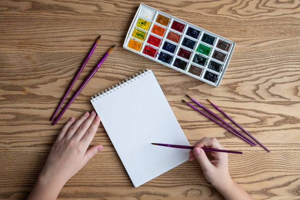 Aquarelle, papier aquarelle et pinceau sur table en bois, main avec vernis nu - Photo, image