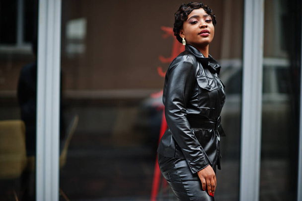 Fashionable beautiful african american woman posing in black leather jacket and pants at street. - 写真・画像