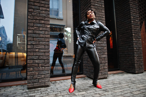 Fashionable beautiful african american woman posing in black leather jacket and pants at street. - Фото, зображення