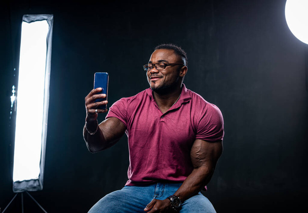 Young handsome african american talks over video connection on black studio background. Led lamps in studio. - Photo, image