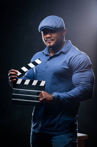 Young muscular african american man holds clipboard on black studio background. Fasion portrait of handsome black man. - Φωτογραφία, εικόνα