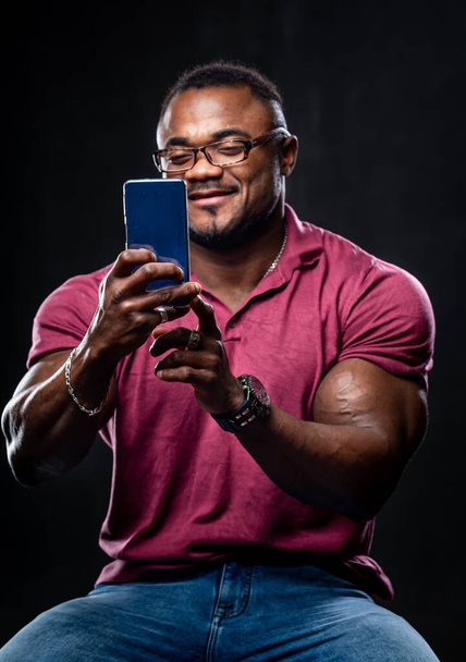Handsome black man takes selfie on phone. African american in pink shirt on black background. Closeup. - Valokuva, kuva