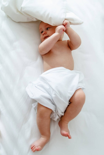 A cute kid lies in a wooden baby bed and plays with a pillow - Fotoğraf, Görsel