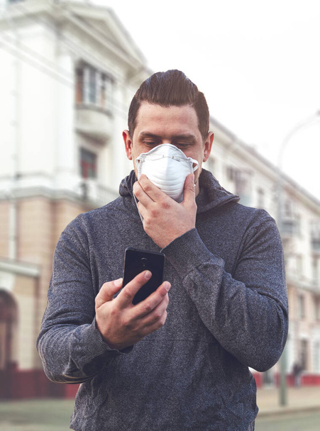 Koronavirüs salgını sırasında ya da hava kirliliği olan bir şehirde koruyucu solunum cihazına bağlı bir adam telefon kullanabilir. Akıllı telefon kullanan bir adam Covid-19 davalarının son haberlerini okuyor. Salgın sırasında iletişim - Fotoğraf, Görsel