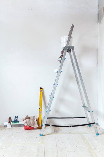 A stepladder with painting tools in a room in a house or apartment. Preparing for putty on the wall or painting. Home repair or renovation concept. - Фото, изображение