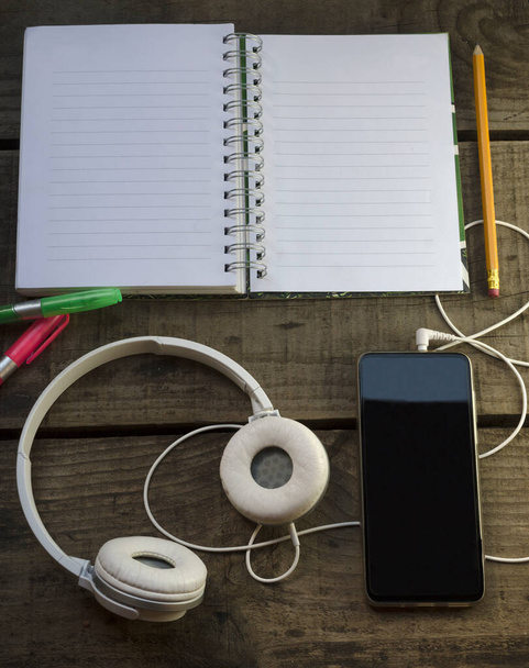 cuadernocon lapiz y resaltadores, telefono para escuchar musicar e inspirarse, sobre mesa de madera - Photo, Image