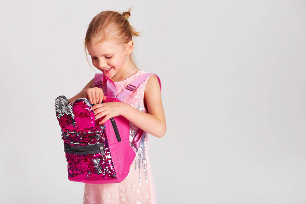 Cute little girl with bunny ears backpack in pink cekinowa sukienka. Dzieciństwo, edukacja i koncepcja ludzi - szczęśliwa dziewczynka z torbą szkolną na szarym tle - Zdjęcie, obraz