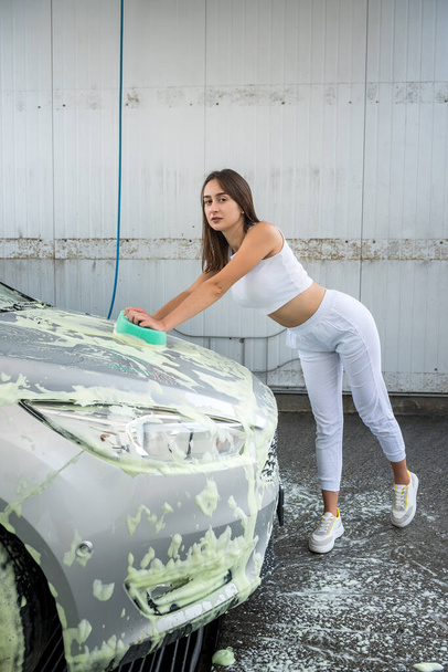 Beautiful woman washes her car with green sponge in foam from dirty  - Фото, зображення