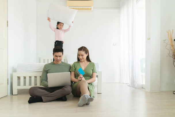 férfi és feleség dolgozik laptop a hálószobában és a lánya áll az ágy mögött, munka otthonról koncepció. - Fotó, kép