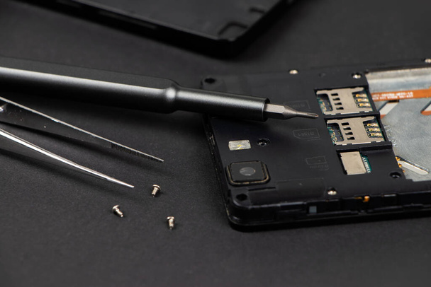 Broken mobile phone and repair tools on dark background, flat lay - Foto, afbeelding