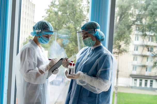 dos jóvenes practicantes trabajan con tubos de ensayo con sangre para la investigación de laboratorio para detectar un nuevo virus peligroso COVID-19 - Foto, Imagen