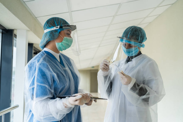 Due medici di sesso femminile con indumenti protettivi tengono provetta con campione di sangue al coronavirus in clinica moderna. pandemia COVID-19 - Foto, immagini