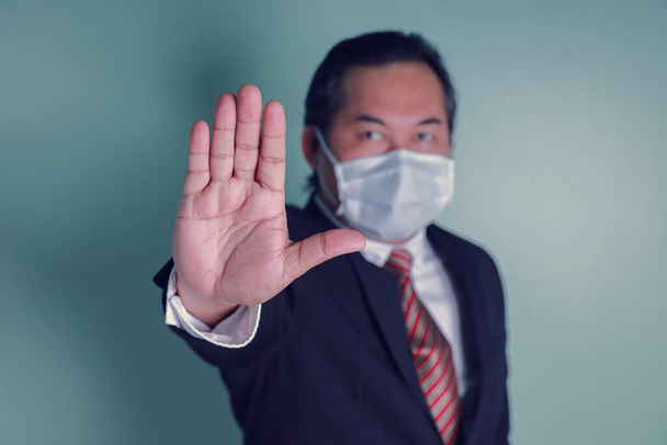 Портрет крупным планом к руке бизнесмена, показывающий знак "стоп". Азиатский портрет бизнесмена носит черный костюм в медицинских масках. Здравоохранение защищает ковид-19. - Фото, изображение