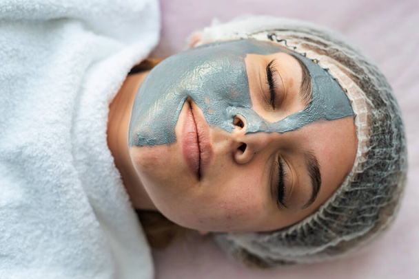 Güzellik kliniğindeki bir yatakta yüz maskesi takan genç bir kadın. Sağlık hizmeti kavramı - Fotoğraf, Görsel