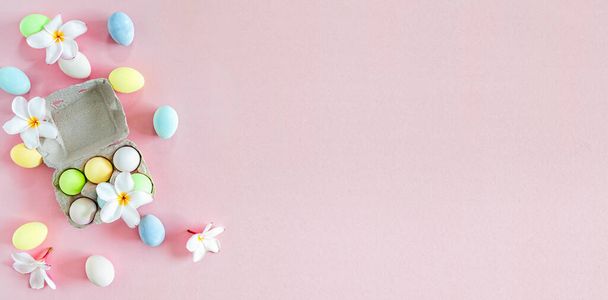 Bunte Pastellfarbene Ostereier mit weißen Frangipani-Blüten auf rosa Hintergrund, Draufsicht mit natürlichem Licht. Flache Verlegestile. - Foto, Bild