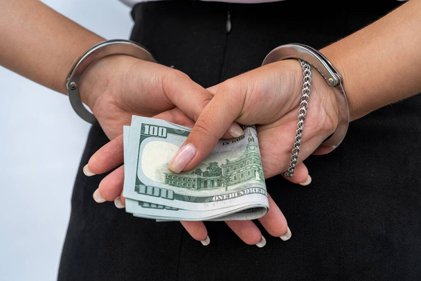 Großaufnahme von weiblichen Händen in Handschellen und Dollarnoten isoliert auf grau. Korruptions- und Bestechungskonzept - Foto, Bild