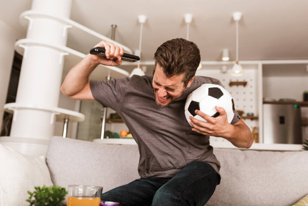 Mladý fotbalový fanoušek muž sleduje fotbalový zápas v televizi v obývacím pokoji gauč. - Fotografie, Obrázek