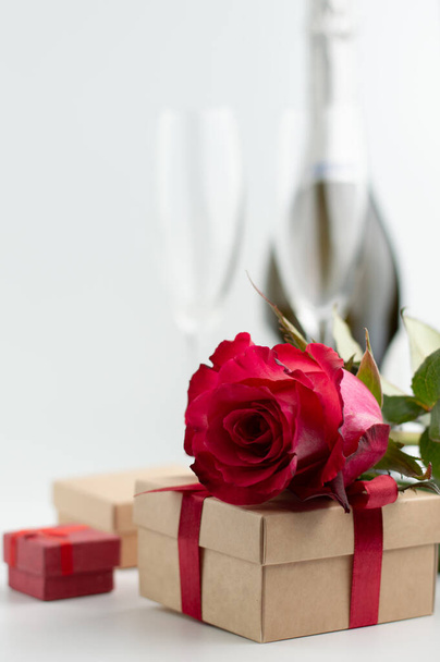 Blurred image of gifts, glasses and a bottle of champagne, in the foreground a rose. Romantic background with bokeh effect. - Foto, afbeelding