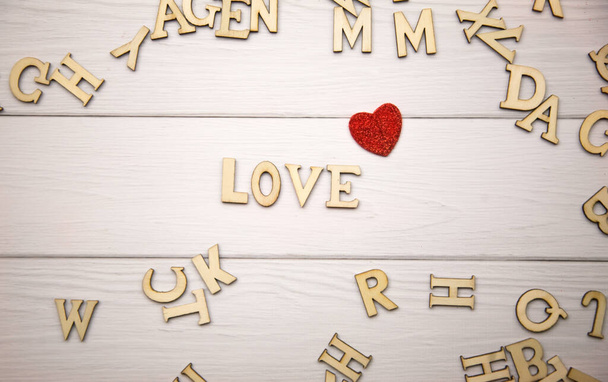 The word love made from decorative wooden letters on a light wooden background with glitter red hearts. Valentine's day poster, greeting card, banner - Fotó, kép