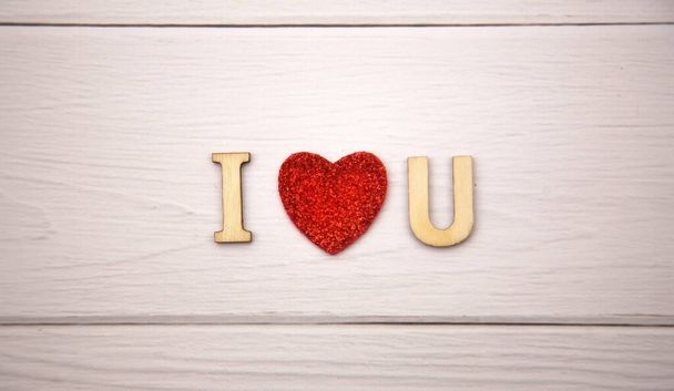 The word i love you made from decorative wooden letters on a light wooden background with glitter red hearts. Valentine's day poster, greeting card, banner - Foto, afbeelding