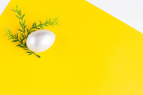 Composizione delle vacanze pasquali. Uovo color argento con un rametto di verdi su un doppio sfondo giallo-bianco. Ley piatto pasquale. Concetto pasquale. Copyspace. - Foto, immagini