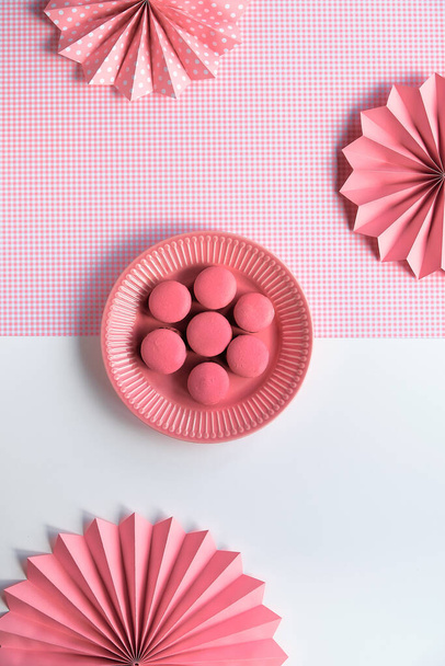 Creative food concept. Sweet and tasty pink macaroons on a plate. Monochrome flat lay on split two tone pink white background with folded paper fans. - Фото, изображение