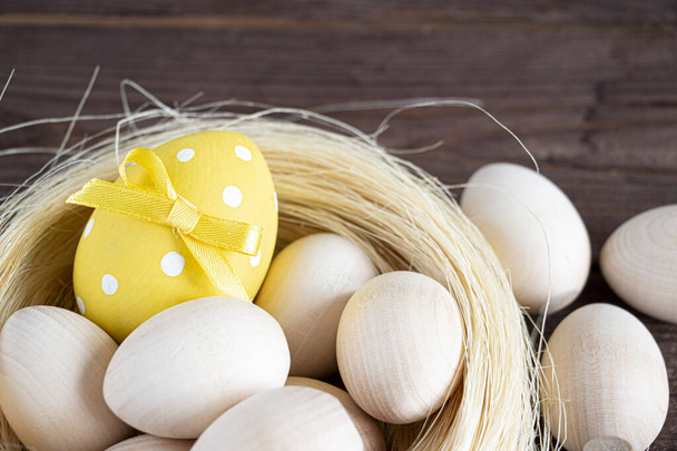 Cartão de Páscoa. Ovos brancos no ninho. Um ovo pintado de amarelo decorado com um arco. Num fundo escuro. Espaço de cópia para texto. - Foto, Imagem