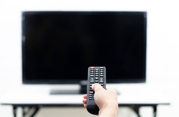 Hand die de afstandsbediening vasthoudt om de TV aan te zetten - Foto, afbeelding