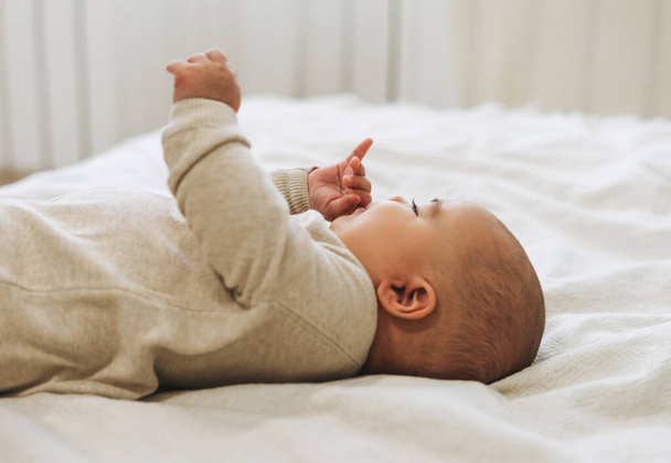 Nettes lächelndes Baby in beige Overall 5-6 Monate auf dem Bett, natürliche Töne - Foto, Bild