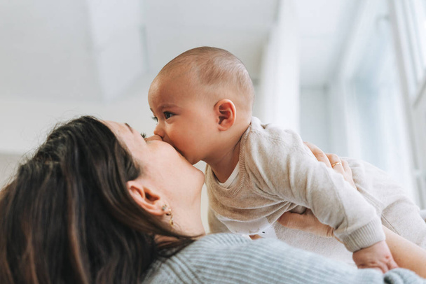 Junge Mutter küsst ihr süßes Baby auf Händen in hellen Raum, Liebe Emotionen - Foto, Bild