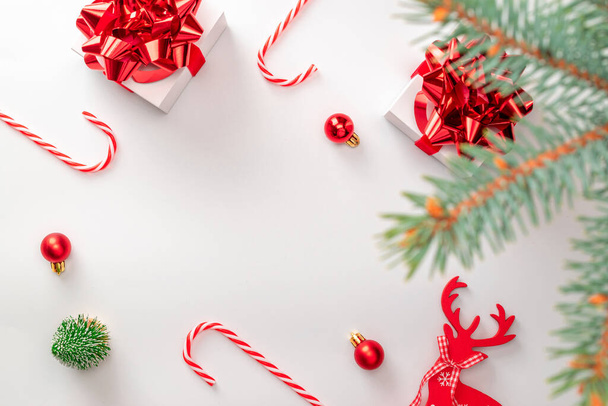 Zimowy design. Białe pudełko z czerwoną wstążką, piłeczki noworoczne, cukierki i musujące światła w kompozycji świątecznej na białym tle dla kartki okolicznościowej. Świąteczne tło z miejscem na tekst - Zdjęcie, obraz