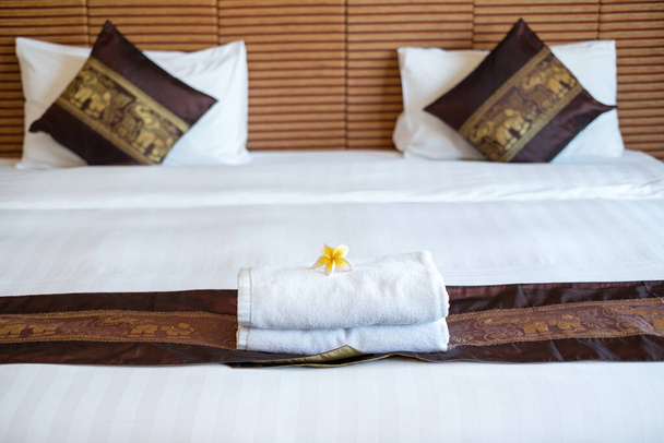 Una sirvienta del hotel apiló toallas en la cama y colocó flores en las toallas en una habitación de hotel.. - Foto, Imagen