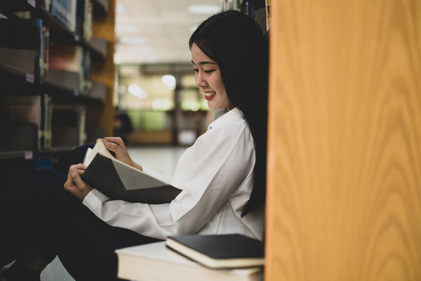 Молодые азиатские женщины ищут книги и читают книги на столах и проходах университетских библиотек для исследования и развития академического и образовательного самосознания.. - Фото, изображение