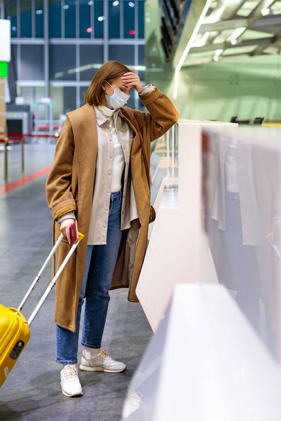 Frau mit verärgertem Gepäck über Flugausfall, steht wegen Reisebeschränkungen durch Coronavirus-Pandemie / Covid-19-Ausbruch an leeren Check-in-Schaltern im Flughafenterminal. Quarantäne-Maßnahmen.  - Foto, Bild