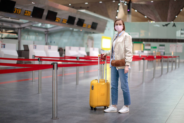 Vrouw met bagage staat bij bijna lege check-in balies op de luchthaven terminal als gevolg van coronavirus pandemie / Covid-19. Vluchtannulering. Financiële crisis in de reisindustrie, wereldwijde recessie.  - Foto, afbeelding