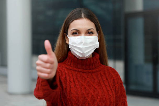 COVID-19 Αισιόδοξη νεαρή γυναίκα με προστατευτική μάσκα που δείχνει τους αντίχειρες της στον δρόμο της πόλης έτοιμη για την εκστρατεία εμβολιασμού κατά της νόσου του Coronavirus 2019 (Sars-Cov-2) - Φωτογραφία, εικόνα
