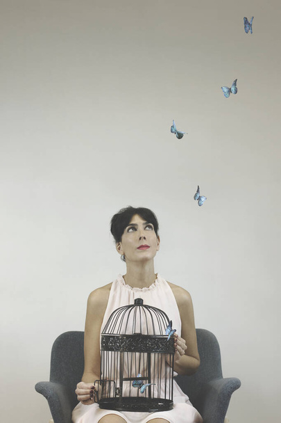 foto conceptual de la libertad con una mujer joven liberando mariposas de arte de colores de una jaula - Foto, Imagen