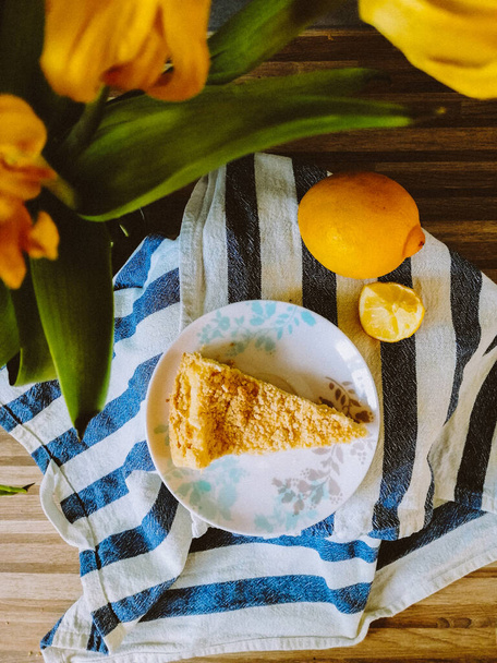 Gesunder Quark-Käsekuchen mit süßer Zitronensauce auf dem weißen Teller vor dem Hintergrund gelber Tulpen und Zitronen - Foto, Bild