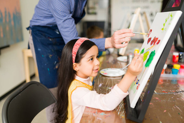 子供のための彼女の芸術のクラスの間にキャンバス上できれいな絵を描く美しい小学生の側面図  - 写真・画像