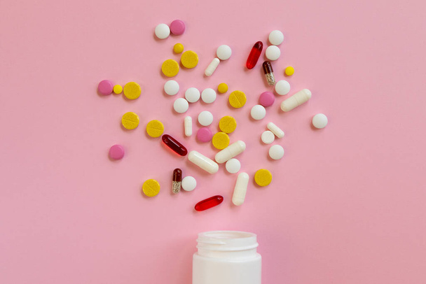 Pillole mediche assortite e capsule sparse da una bottiglia di plastica bianca su uno sfondo rosa. Concetto di trattamento per un malato. Vista dall'alto. Posa piatta. - Foto, immagini