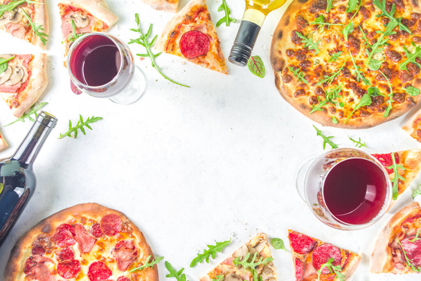 Pizza-Party-Konzept. Pizzen mit verschiedenen Füllungen, verschiedene Pizzastücke, Glas und Flasche mit Wein. Flache Ansicht Kopierraum auf weißem Hintergrund - Foto, Bild
