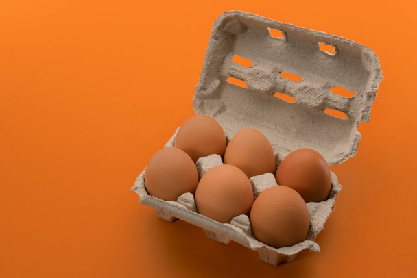 Яйцо коробка с яйцами, шесть куриных яиц в картонный лоток яйцо из переработанной бумаги изолированы на оранжевом фоне  - Фото, изображение