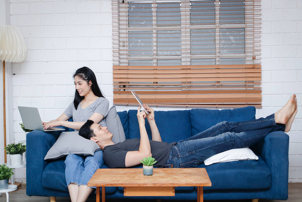 Azjatycka młoda para Usiądź i zrelaksuj się na niebieskiej kanapie w ich domu podczas wakacji. Koncepcja rodzinna, praca w domu. przestrzeń kopiowania - Zdjęcie, obraz