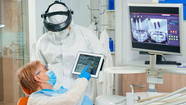 Estomatólogo con escudo facial revisando rayos X apuntando en la tableta - Foto, imagen