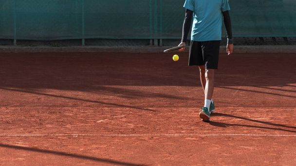 Tennis player on red clay court prepares to serve. Athlete with tennis racket and ball. Start of match, game, set. Sports panoramic background or banner with copy space - Photo, Image