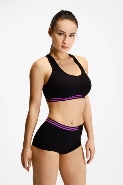 Athletic young woman in black sportswear posing over white background - Fotó, kép