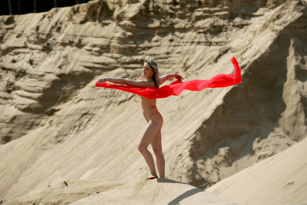 Krásná nahá žena s červeným materiálem pózující v pozadí hory písku - Fotografie, Obrázek