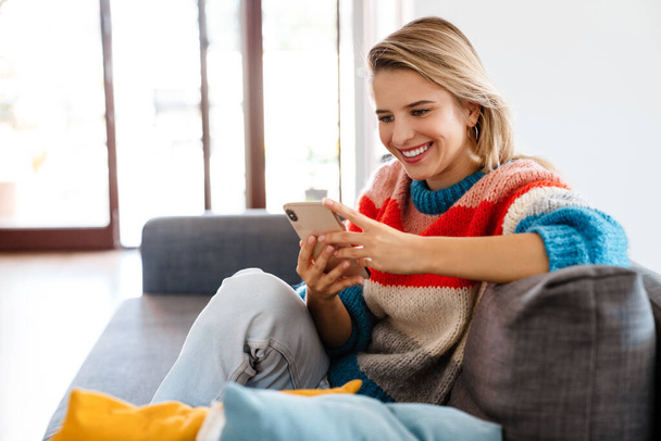 Happy girl reading a message in a smart phone sitting on a couch at home - Фото, изображение