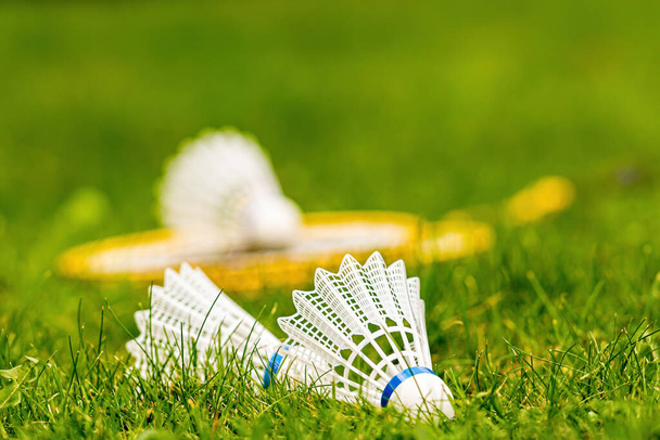 white shuttlecock close-up in a green meadow with yellow badminton rackets against a blurred background - Foto, Imagen